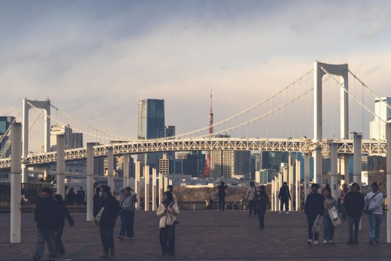 Beautiful sunset view of Rainbow Bridge and Tokyo skyline with people strolling on a promenade.