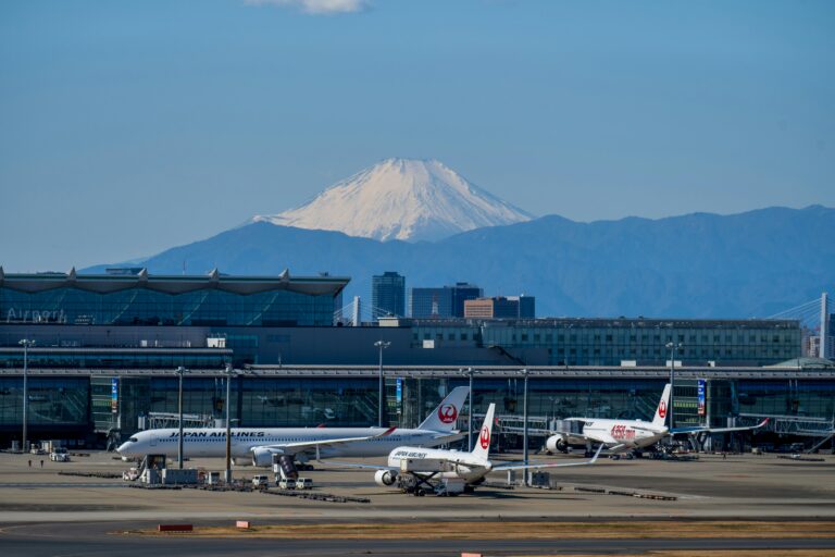 A bustling scene at Haneda Airport with airplanes and Mount Fuji in the background.