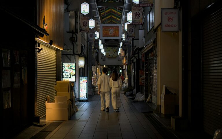 A couple in matching outfits walks through Kyoto's Nishiki Market at night, highlighting urban nightlife.